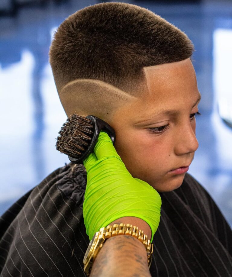 Barber using a soft brush to clean off a young client after a fresh haircut with a creative curved hair design.